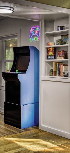 A room with a blue arcade machine, a neon sign, and a bookshelf with various items.