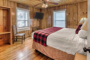 A wooden cabin room with a bed, a chair, a television, and a window. - Poppy’s Outpost • Hot Tub • Fire Pit • Family Fun (Cosby)