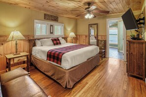 A bedroom with a wooden ceiling, a bed with a red and black checkered blanket, two bedside lamps, and a ceiling fan.
