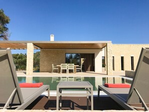 A modern outdoor pool area with lounge chairs and a table, surrounded by stone walls and a clear blue sky. - Villa Demeter - Three Bedroom Villa, Sleeps 6 (Ionian Islands)
