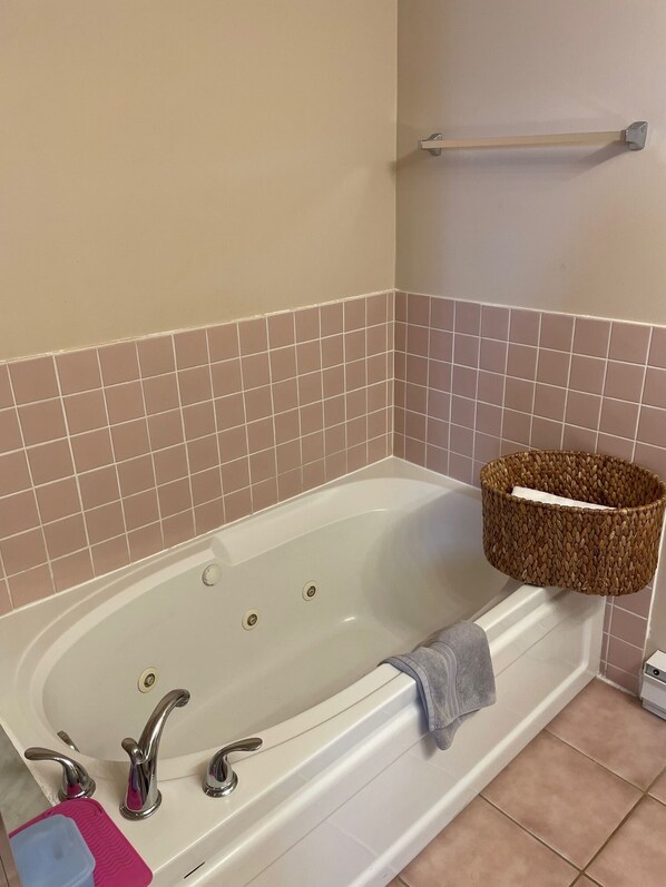 A bathroom with a white bathtub, beige tiles, a towel rack, and a woven basket.