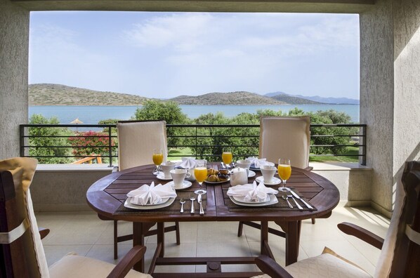 A round wooden table set for breakfast with a scenic view of hills and water.
