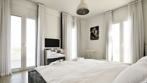 Ein modernes Hotelzimmer mit einem großen Bett, einem Flachbildfernseher, einem kleinen Tisch und Blick ins Freie durch große Fenster.
