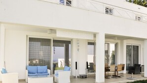 Ein modernes Gebäude mit überdachter Außenbereichgestaltung, ausgestattet mit weißen Sofas und Sesseln, einem Esstisch und einem kleinen Tisch mit Kerze.