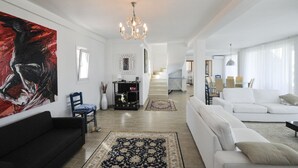 Ein geräumiges Wohnzimmer mit einem großen, abstrakten Gemälde, einer Chandelüster und einer Treppe, die zu einer weiteren Ebene führt.