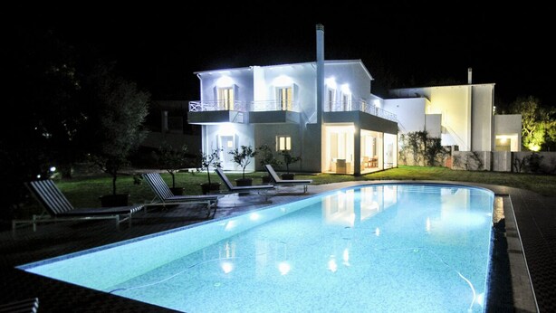Ein modernes Haus mit Schwimmbad, Liegestühlen und einer gut beleuchteten Außenfassade bei Nacht.