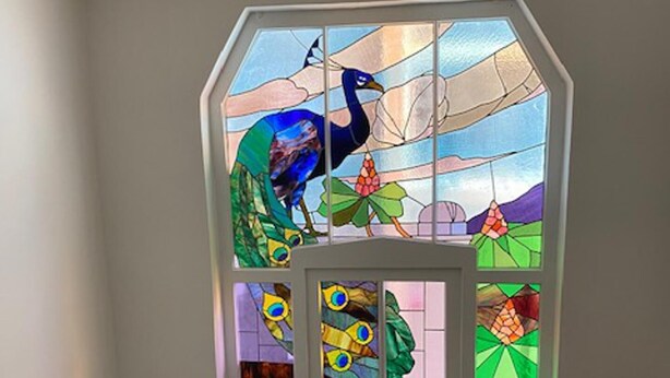 A stained glass window with a peacock design, a white door, and a small window with a geometric pattern.
