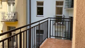 A multi-story residential building with balconies, a tiled balcony floor, and a clear view of the adjacent building.