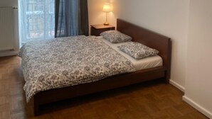 A bedroom with a bed, a nightstand, a lamp, and a window with curtains.