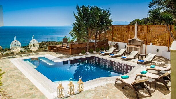 Un área de piscina con vista despejada al mar, sillas de descanso y una terraza de madera.