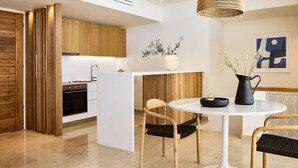 A modern kitchen with wooden cabinets, a white island, and a dining area with a round table and chairs. - Thalassa Villas - Three-Bedroomed Private Pool Seafront (Agios Nikolaos)