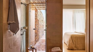 A bathroom with a shower, a towel hanging on the wall, and a small table with a tray and a bottle. - Thalassa Villas - Three-Bedroomed Private Pool Seafront (Agios Nikolaos)