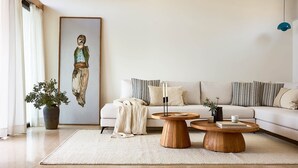 A modern living room with a sofa, two wooden coffee tables, a large potted plant, and a framed artwork. - Thalassa Villas - Three-Bedroomed Private Pool Seafront (Agios Nikolaos)