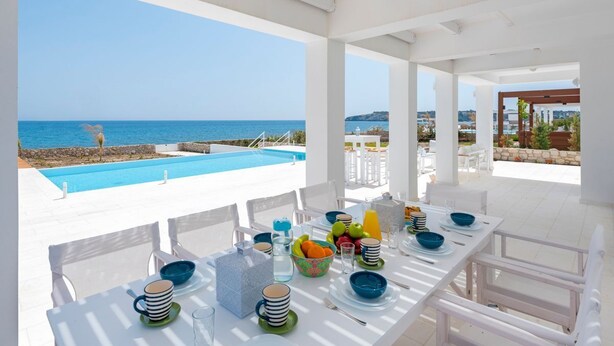 A dining area with a view of the sea, white furniture, and a pool. - Villa Constantine - Six Bedroom Villa, Sleeps 15 (Kolympia)