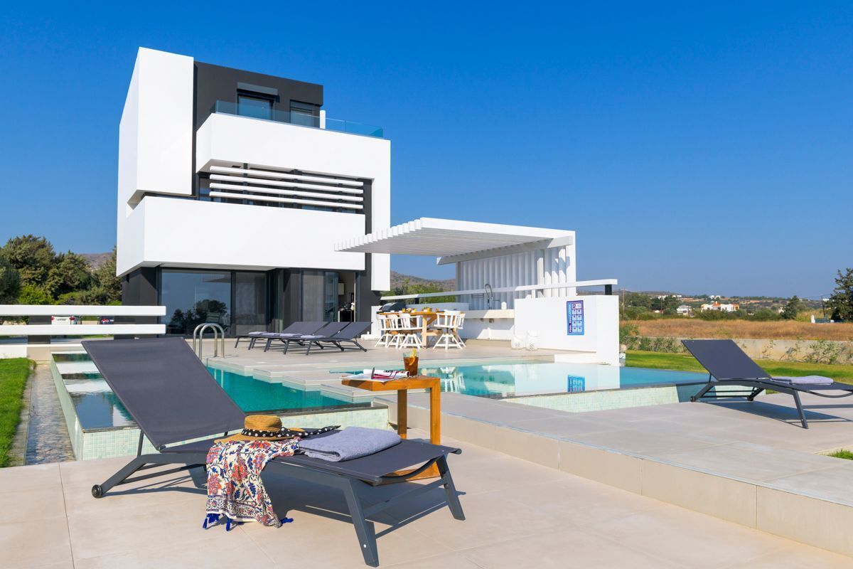 A modern villa with a swimming pool, sun loungers, and a dining area.