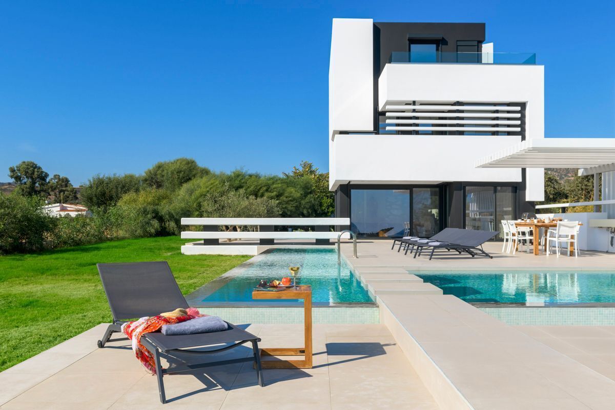 A modern two-story house with a swimming pool, outdoor seating, and a view of the surrounding greenery.