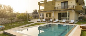 Un edificio de dos pisos con piscina, mobiliario exterior y vistas del paisaje circundante.