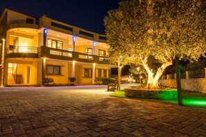 Un hotel de varios pisos con balcones, un patio empedrado y un árbol bien iluminado.