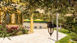A paved patio area with outdoor seating, a stone wall, and greenery. - Villa Chorio - Four Bedroom Villa, Sleeps 8 (Afandou)