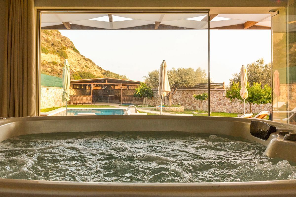 A hot tub with a view of a pool and outdoor seating area.