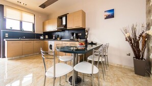 Une cuisine moderne avec un coin repas, comprenant une table ronde en verre entourée de quatre chaises, un four encastré et une grande fenêtre.