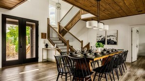 A dining area with a wooden staircase, a large table set for six, and a view of the outdoors. - Swim Spa/Views/Gameroom/Theater/Luxe Design - Rabbit Run (Gatlinburg)