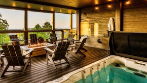 A hot tub area with lounge chairs and a table, surrounded by large windows offering a view of the outdoors. - Swim Spa/Views/Gameroom/Theater/Luxe Design - Rabbit Run (Gatlinburg)