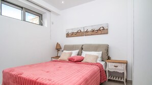 Een slaapkamer met een bed, nachtkastje, lamp en een kunstwerk aan de muur.