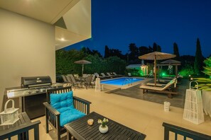 Une terrasse extérieure avec une piscine, des chaises longues, un barbecue et des parasols.