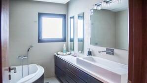 Une salle de bain moderne avec une baignoire, un grand meuble-lavabo avec un miroir et une fenêtre laissant entrer la lumière naturelle.