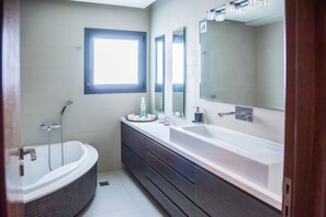 Une salle de bain moderne avec une baignoire, un grand meuble-lavabo avec un miroir et une fenêtre laissant entrer la lumière naturelle.