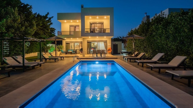 Una moderna casa a due piani con piscina, area salotto esterna e un patio ben illuminato.