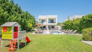 Una moderna casa a due piani con piscina, area salotto esterna e spazio giochi per bambini.