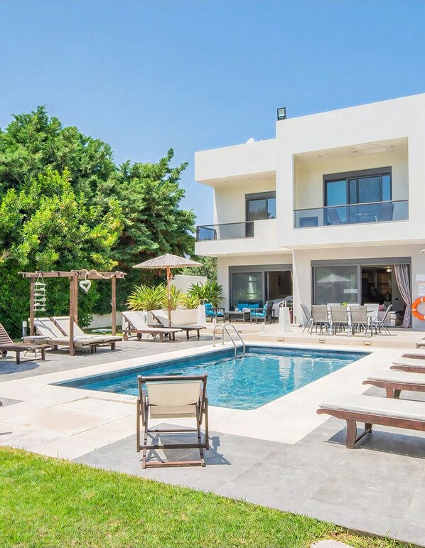 Un hôtel moderne doté d’une piscine, de chaises longues et d’un bâtiment à deux étages.