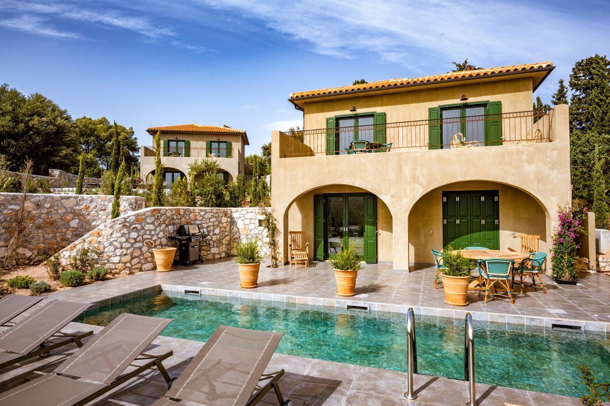 A two-story house with a swimming pool, outdoor furniture, and a stone wall.
