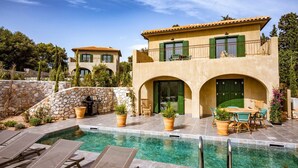 Une maison à deux étages avec une piscine, du mobilier d’extérieur et un mur en pierre.