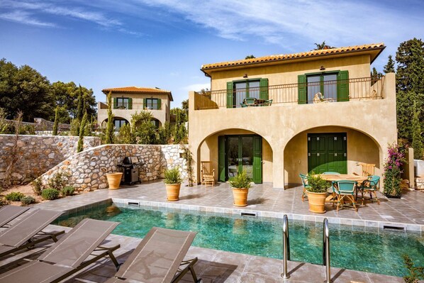 A two-story house with a swimming pool, outdoor furniture, and a stone wall.