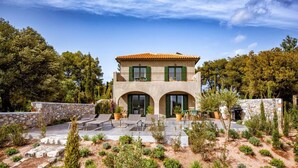 Une maison à deux étages, avec une façade en pierre, des volets verts et un toit recouvert de tuiles.