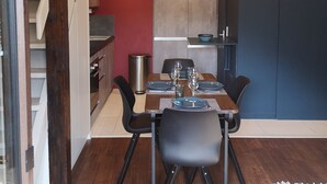 Comedor con mesa de madera dispuesta para cuatro, pared de acento roja y vistas a una cocina y una escalera.