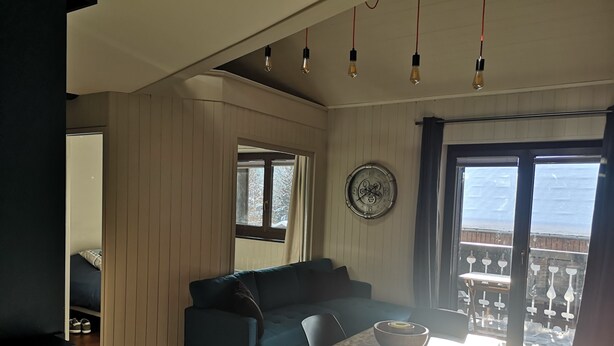 Una sala de estar moderna con un sofá azul oscuro, una mesa blanca con un cuenco y vistas a un balcón con mobiliario exterior.