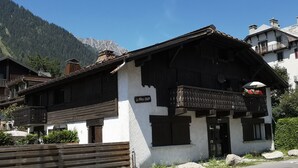 Una cabaña tradicional con un balcón de madera, un cartel que dice "Le Vieux Chalet" y un paisaje de montaña al fondo.