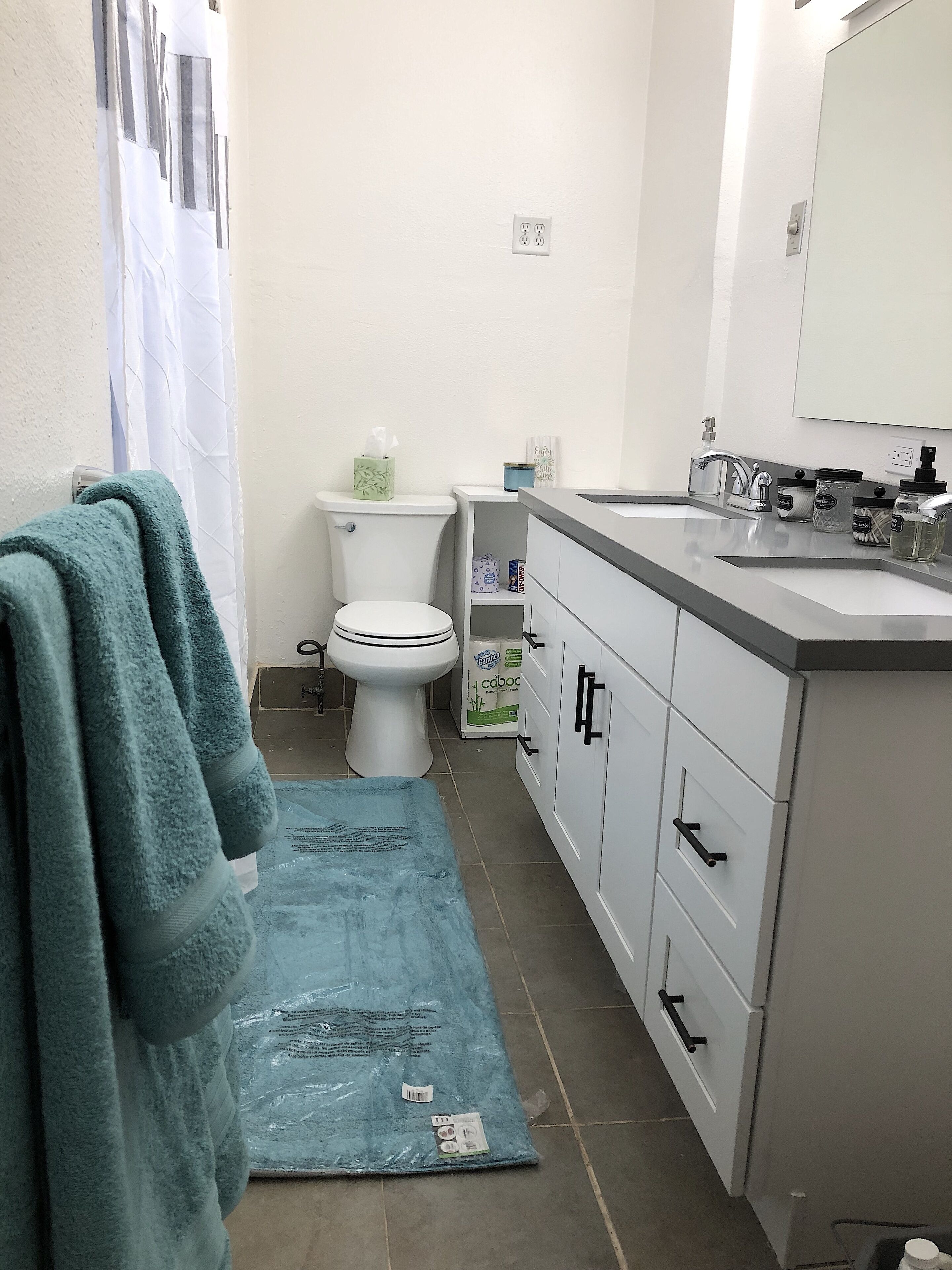 Un bagno con WC, lavandino, mobiletto e un tappetino blu sul pavimento.