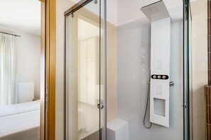 Ein modernes Badezimmer mit einer Duschkabine aus Glas, einer weißen Toilette und einem Bett mit weißer Bettdecke.