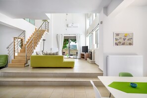 A modern living room with a staircase, a green sofa, and a dining area with a table and chairs. - Skouloufia Villas 1 - Three Bedroom Villa, Sleeps 8 (Roupes)