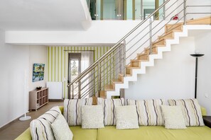 Ein modernes Wohnzimmer mit einem grünen Sofa, gestreiften Kissen, einer Treppe mit Metallgeländern und Blick ins Freie.
