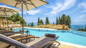 A poolside area with lounge chairs, umbrellas, and a view of the sea. - Empress Sissi - Seven Bedroom Villa, Sleeps 14 (Gastouri)