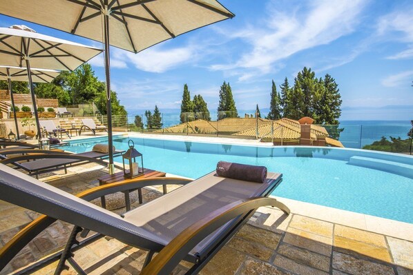 A poolside area with lounge chairs, umbrellas, and a view of the sea.