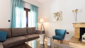 Una sala moderna con un sofá marrón, un sillón azul, una mesa de centro de cristal y una chimenea.