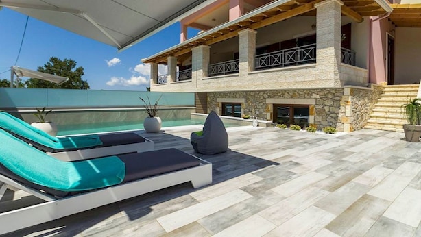 Un área de piscina exterior moderna con sillones de descanso y un edificio de piedra al fondo.