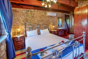 Un dormitorio con pared de ladrillo, estructura de cama de madera, mesita de noche, cómoda y espejo.